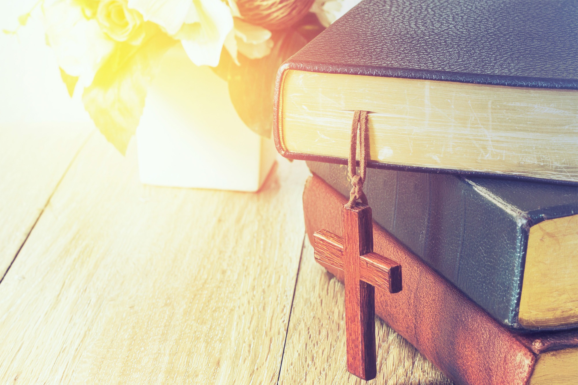 Three stacked books with a wooden cross hanging from the top book
