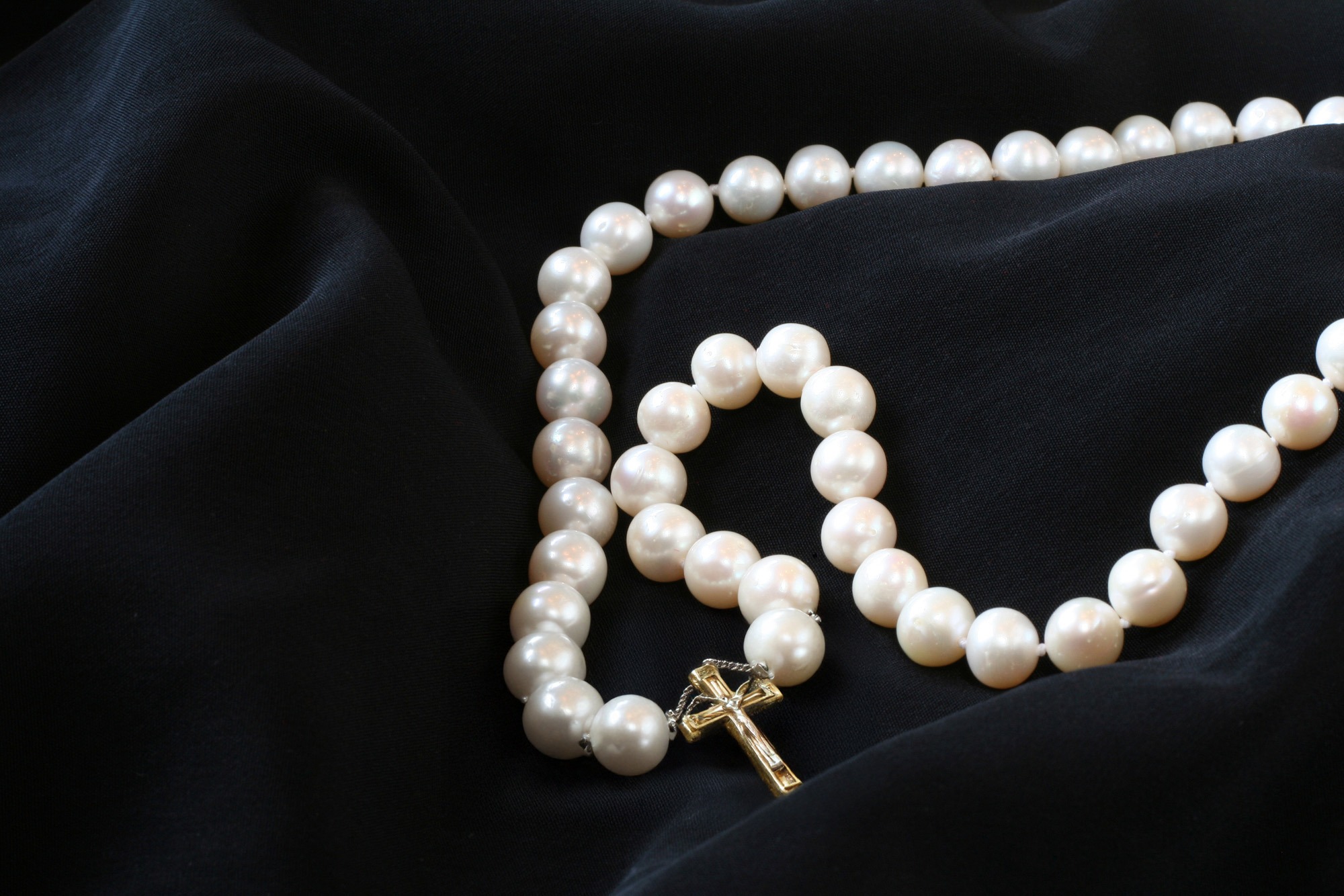 A pearl rosary lays elegantly on black fabric, featuring a golden cross