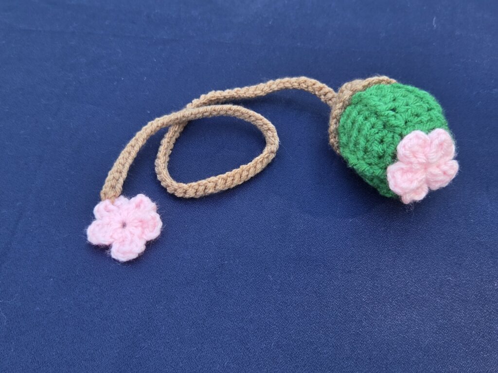 Crochet bookmark, bright green cactus with pink flower on top. Light brown string with additional pink flower on bottom.