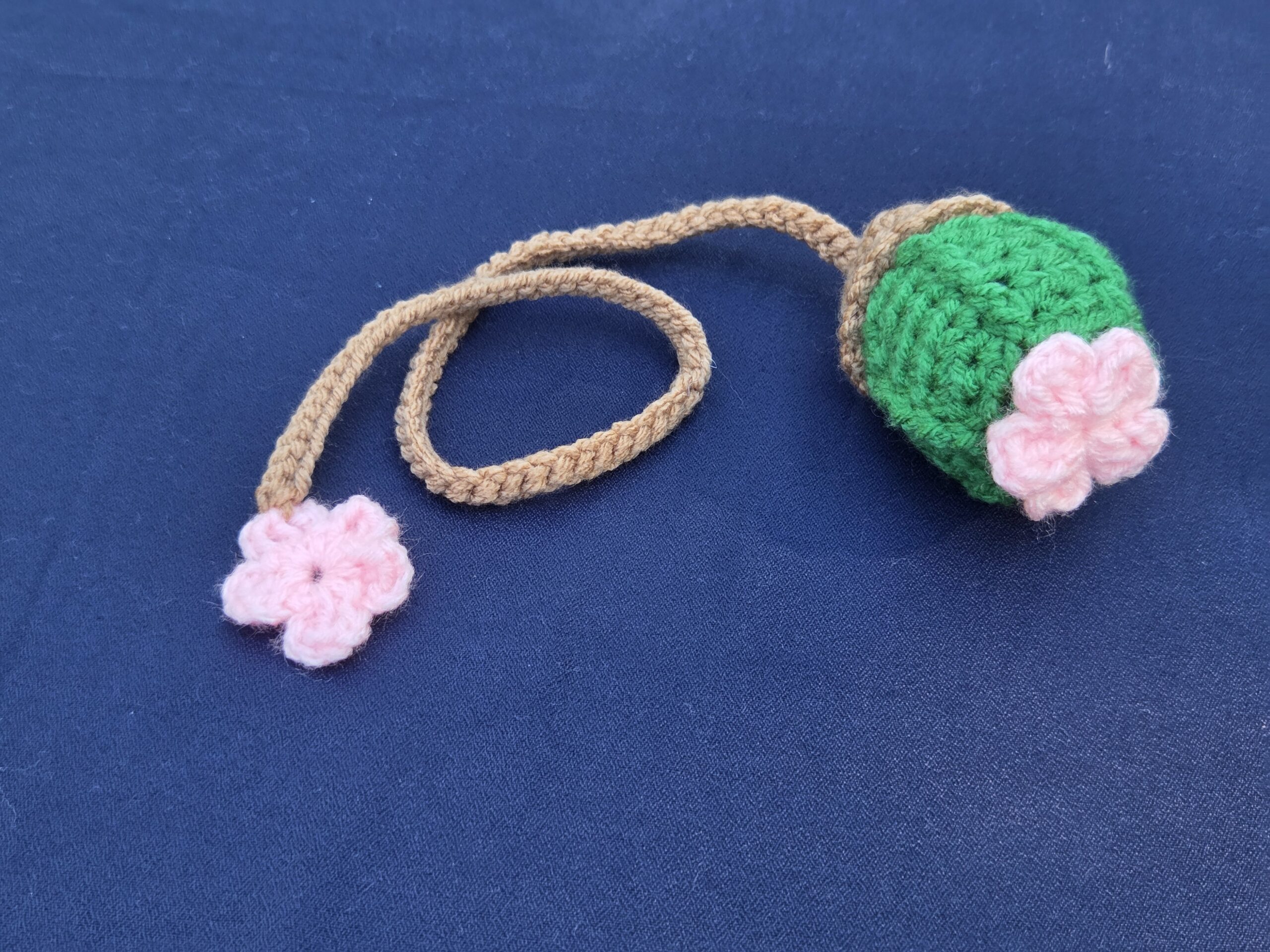 Crochet bookmark, bright green cactus with pink flower on top. Light brown string with additional pink flower on bottom.