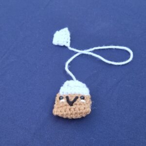 Crochet bookmark looks like a smiling tea bag. Brown and white with cute smiley face and safety eyes.