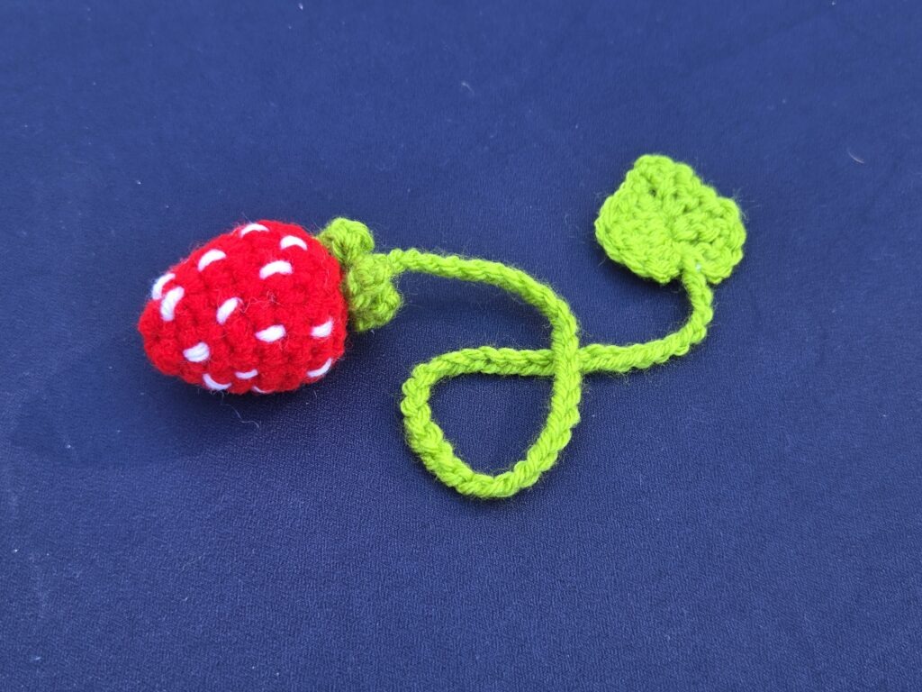 Crocheted strawberry bookmark. Bright red strawberry adorned with tiny white seets. 15" crochet stem, embellished with a grass green leaf on the bottom of the bookmark.