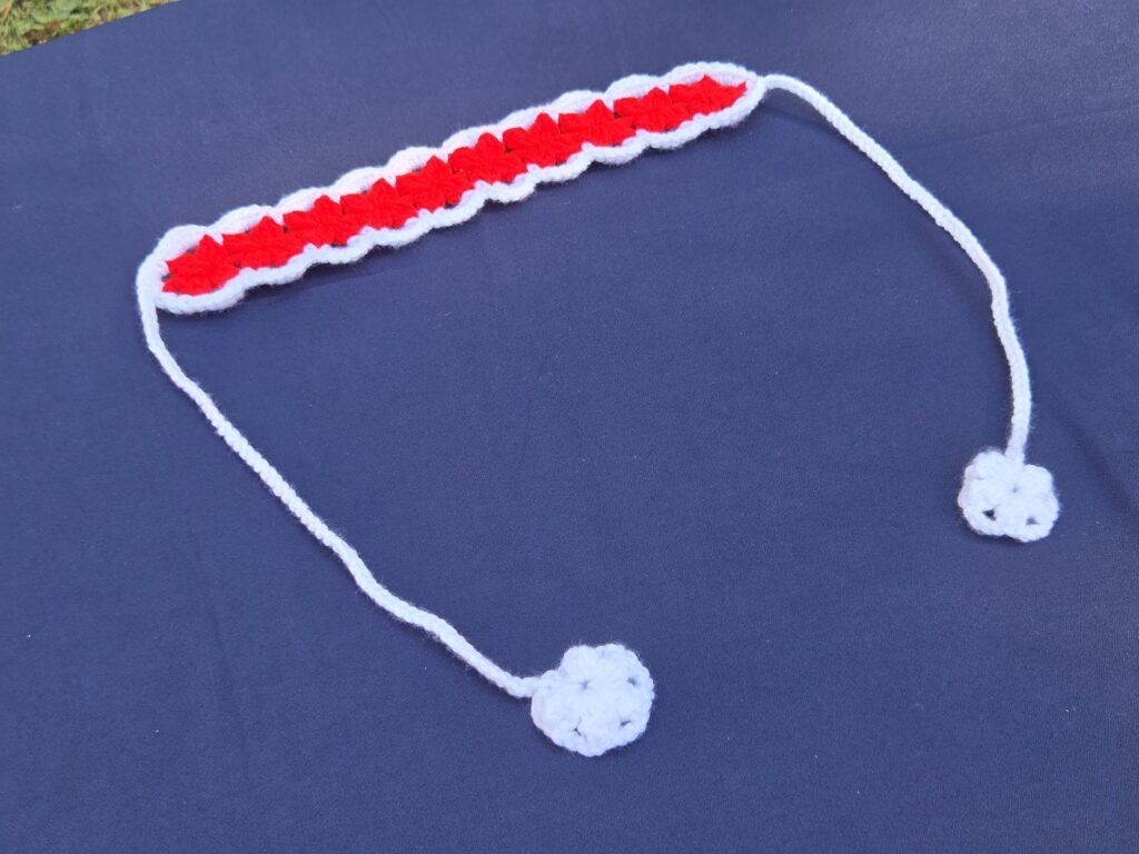 Red and white crochet headband. Band 12 1/2 inches long, 2 inches wide. Straps approx. 14 inches long, featuring white detailed crochet on the ends.