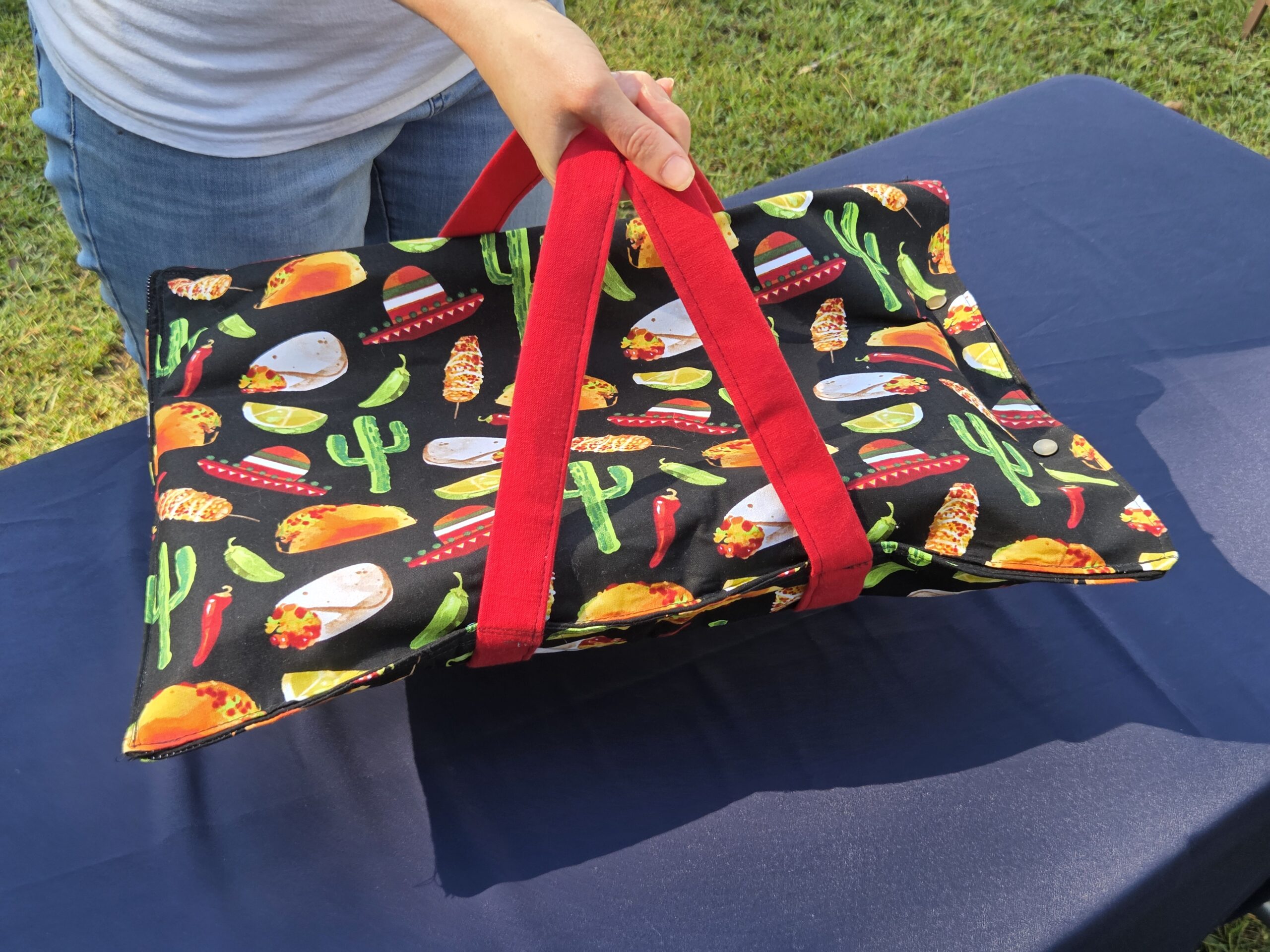 Casserole tote, black with red trim, Mexican print with tacos, burritos, cacti, etc. Double straps with metal snaps. Holds large casserole. Insulated, fully lined.
