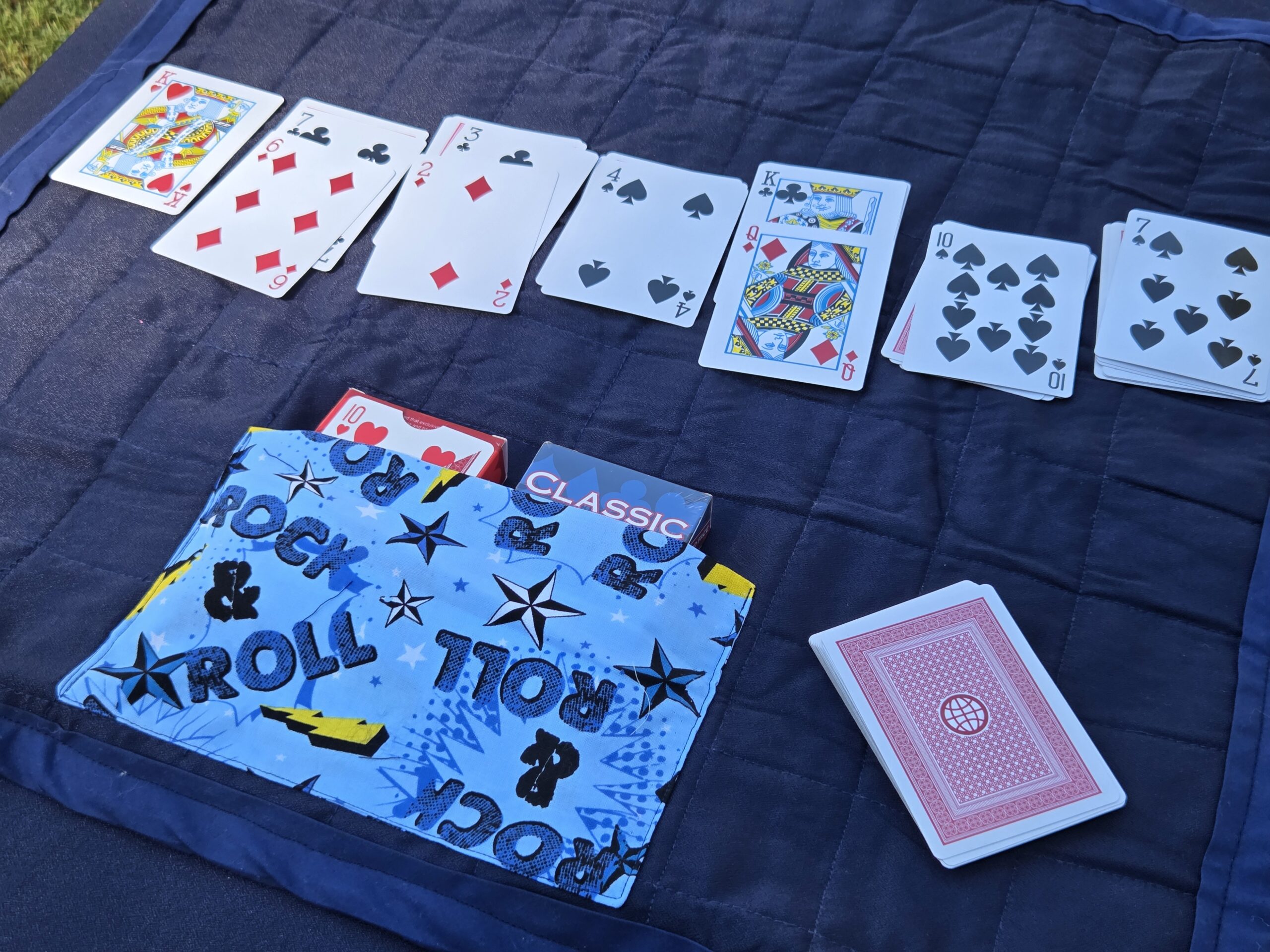 Card carrying case and travel play mat. Rolls up to store up to 2 decks of cards. Rolls out to create a playing surface perfect for Uno, Solitaire, and more. Blue print with rock-and-roll lettering.