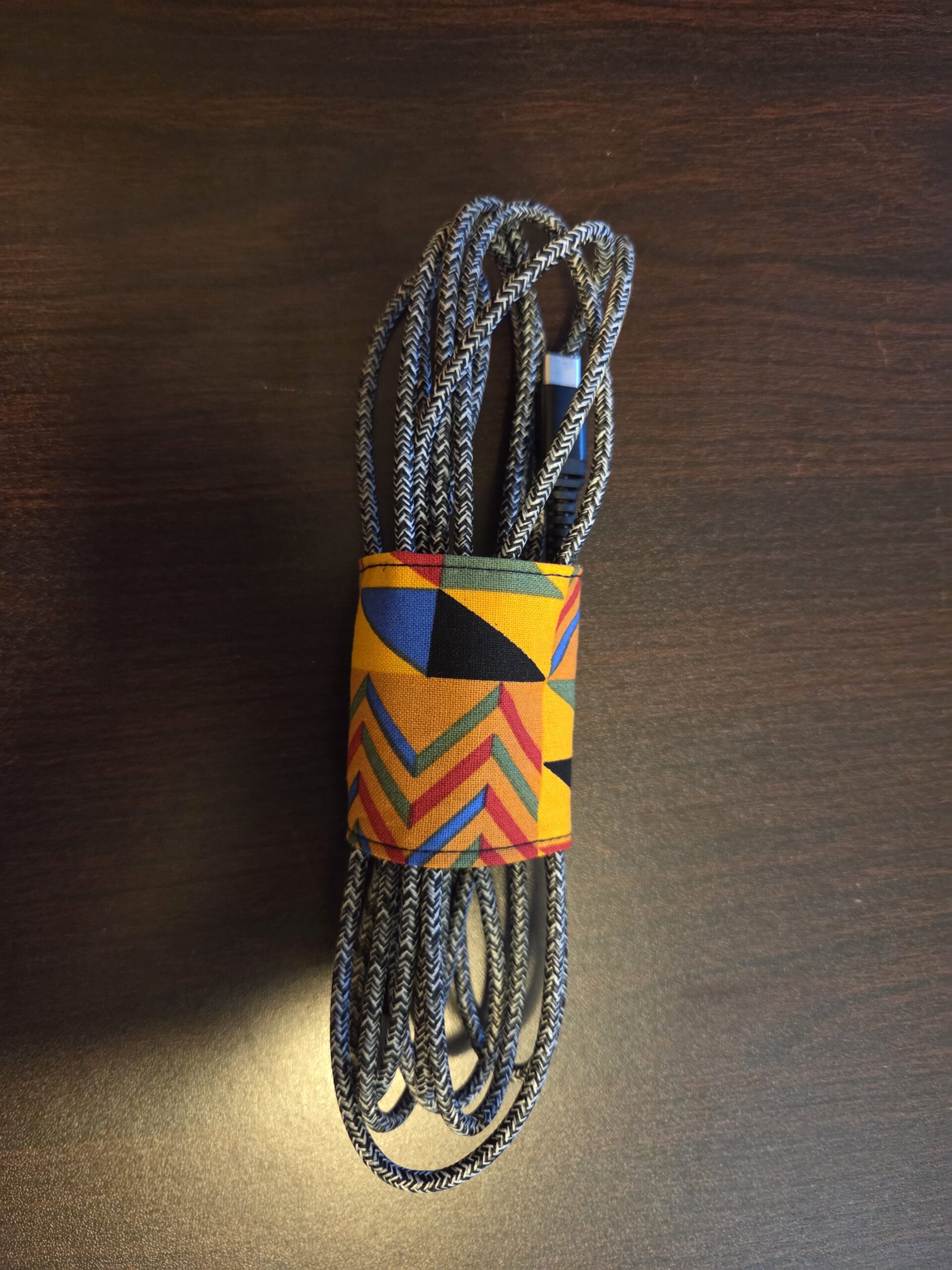 Cord keeper, jeweltones: gold with black, blue, red, and green geometric patterns, black Velcro closure.