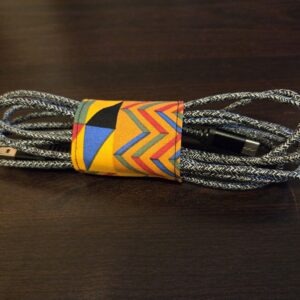 Wrap for keeping electronics cords. Jeweltones: deep gold with black, blue, red, and green geometric designs. Black Velcro enclosure. Sized for cell, tablet, or laptop cords. Cord shown not included.
