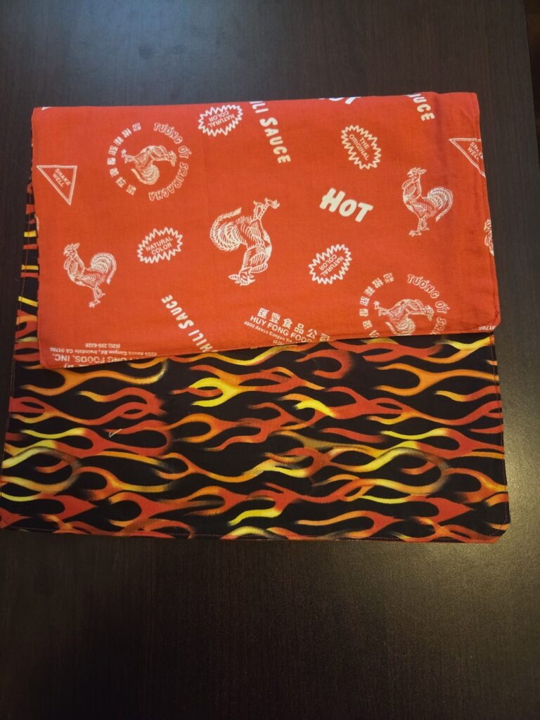 Reversible placemats, set of 4. Top side features red, yellow, and orange flames on black; bottom features Sriracha hot chili sauce print.