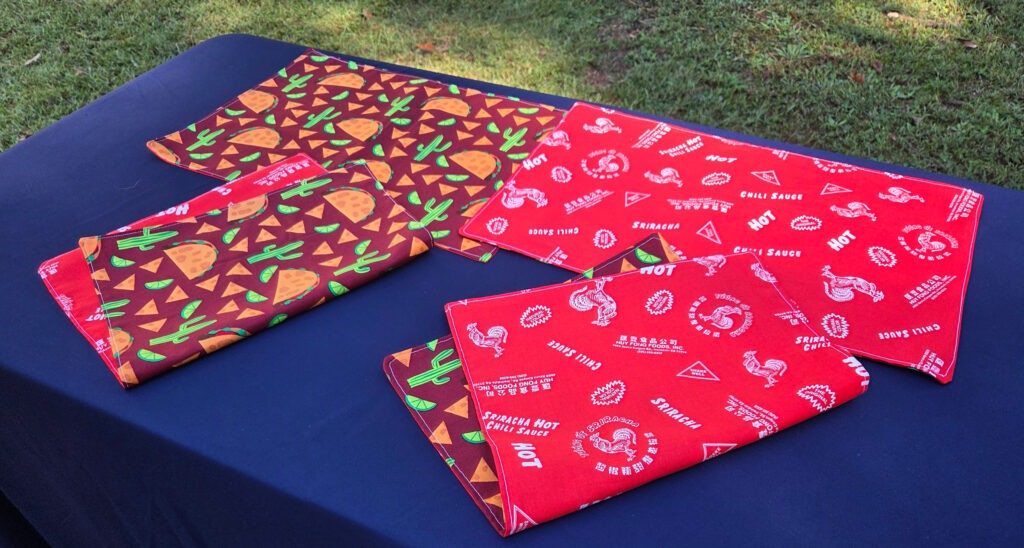 Taco Tuesday set of 4 placemats. Cotton, reversible. Top features tacos, chips, cacti, and lime slices. Bottom features Sriracha hot chili sauce logo.