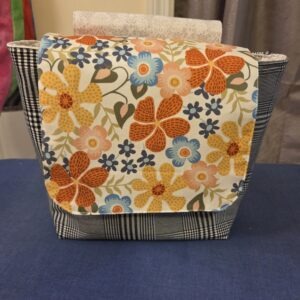 Hanging Messenger Bag in black and white plaid with retro floral accent. Metal snap closure. Zippered pocket.