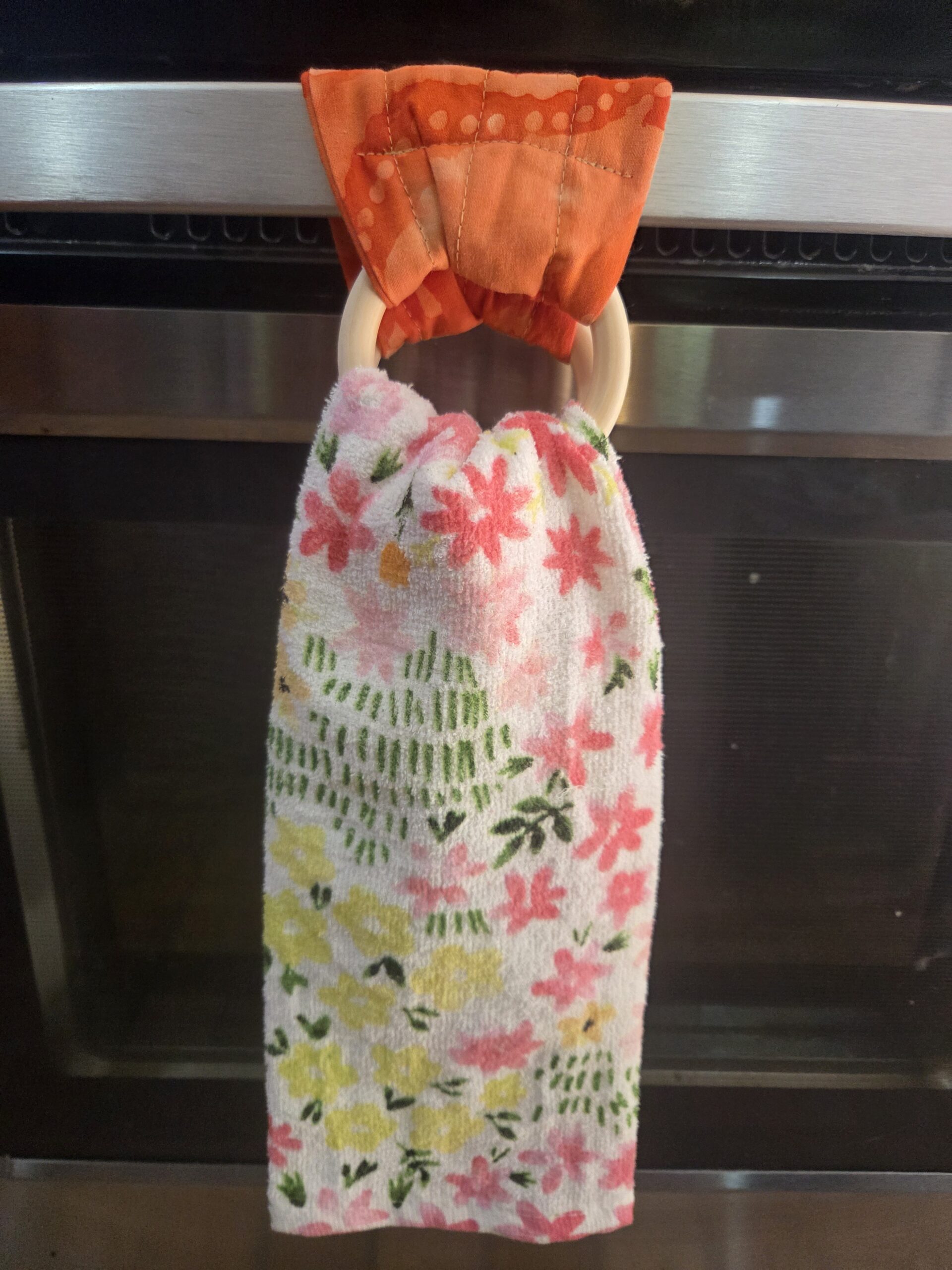 Bright orange kitchen towel hanger with wooden rings.