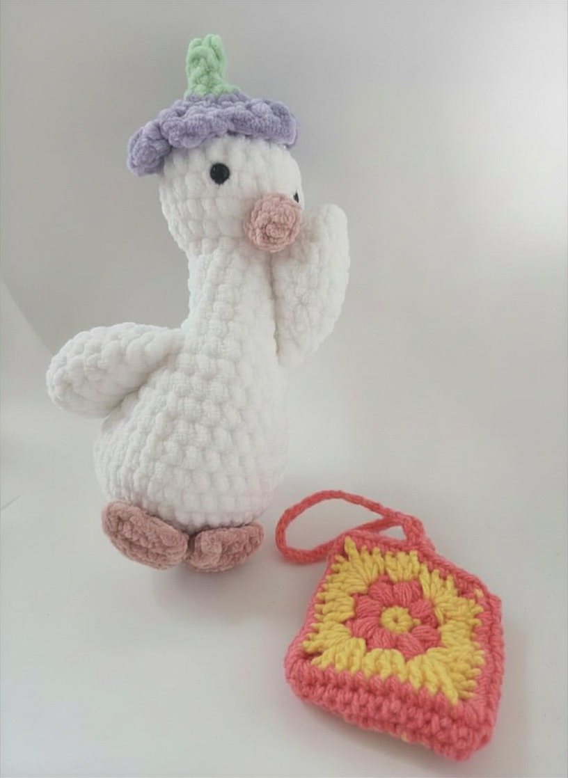 Silly Goose crochet goose wearing a cute purple hat and carrying an adorable orange and yellow handbag.