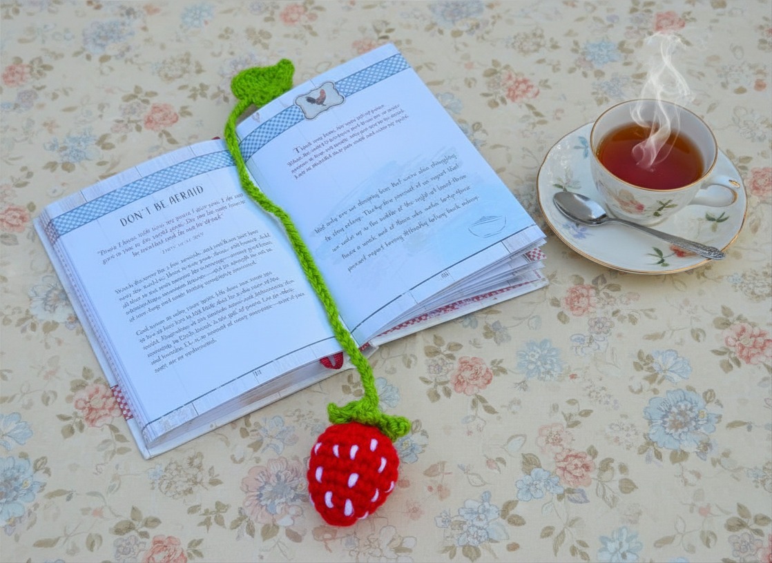 Strawberry bookmark, hand crocheted, bright red strawberry with tiny white "seed" details. Grass-green stem and leaf at the end of the bookmark.