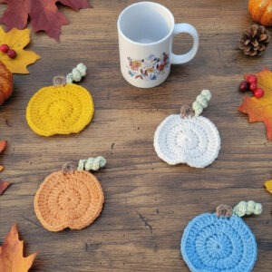 Set of 4 crochet pumpkin coasters in orange, yellow, white, and blue.