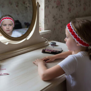 Little girl looking in mirror, wearing a pretty hand crocheted red & white headband.