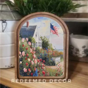 Framed art print on a table showing white beach house with red, white, and blue flowers