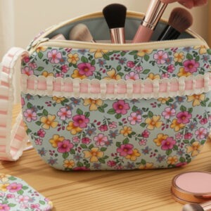 Teacup zipper bag in floral fabric with delicate pink and white ribbon trim. Zip shaped like tea bag. Pink and yellow floral with soft green and blue background.