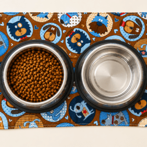 Dog food and water on mat featuring fabric with various breeds of dogs pictured.